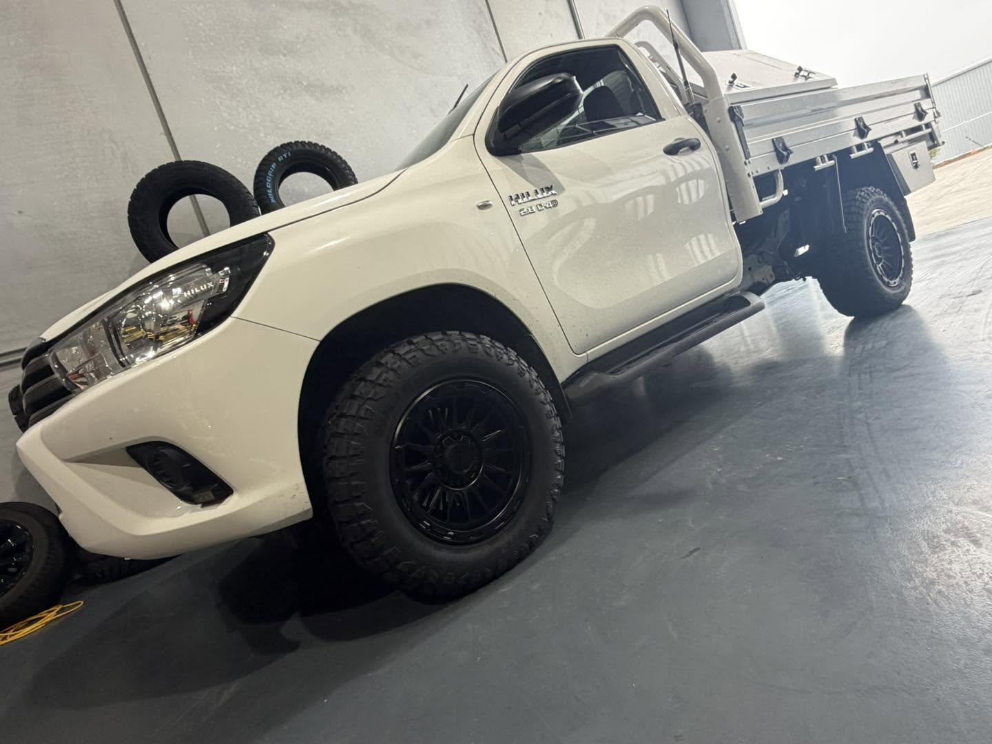 White Toyota HiLux single cab tray ute fitted with black alloy wheels and all-terrain tyres in the Kelso workshop at Australia's Most Wanted Wheels and Tyres Bathurst
